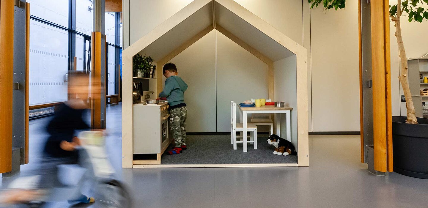 Kind fährt mit einem Laufrad. Im Hintergrund ein weiteres Kind beim spielen. 