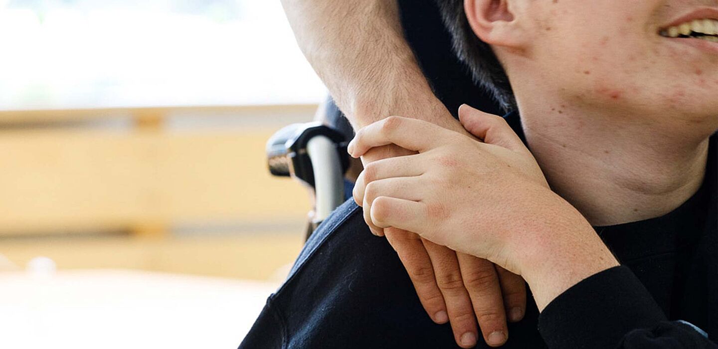 Eine Betreuerin legt einem behinderten Kind die Hand auf die Schulter, das Kind legt seine Hand auf ihre