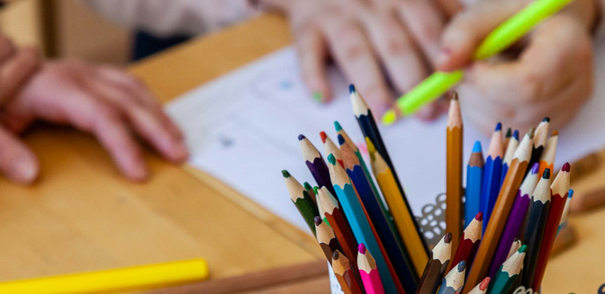 Malstifte im Vordergrund, im Hintergrund malende Kinder