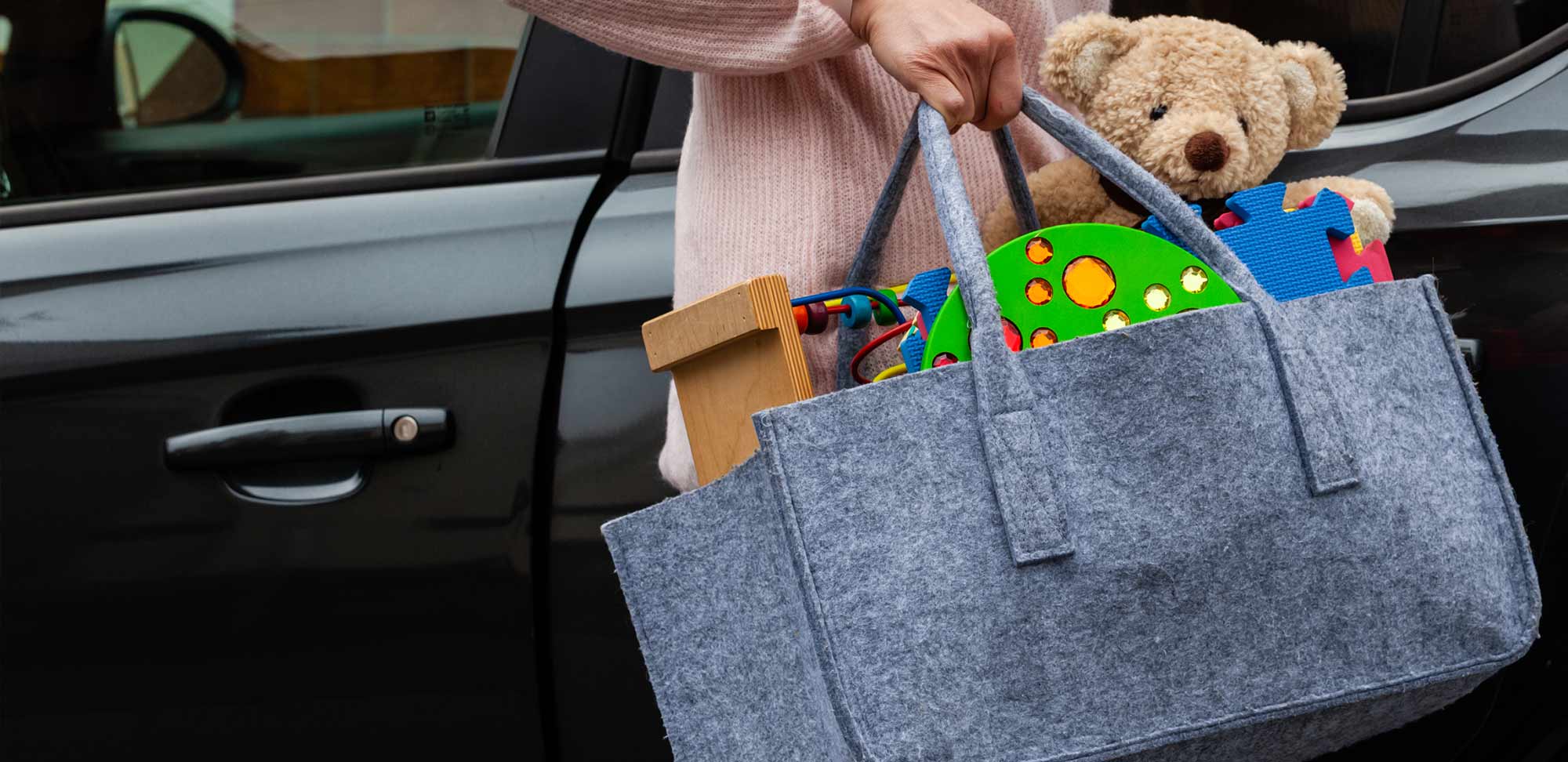 Eine Frau trägt eine Filztragetasche in der Spielzeuge und ein Plüschteddybär sind